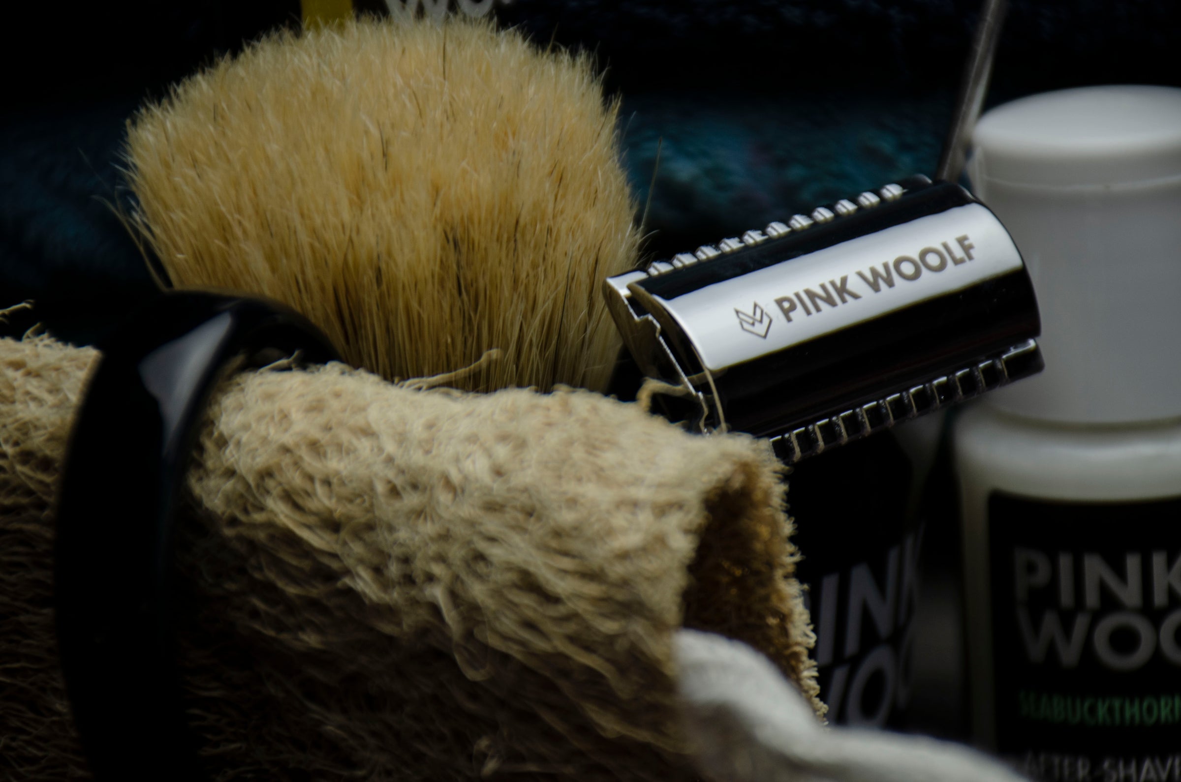 Shaving brush, Seabuckthorn After Shave, safety razor, and Loofa with 'Pink Wool' branding on a dark background with a hand towel