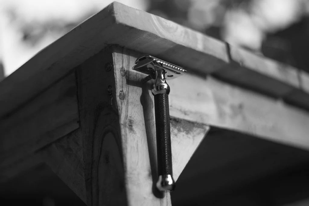 Pink Woolf double edge safety razor resting on a wooden workbench, representing traditional wet shaving craftsmanship.
